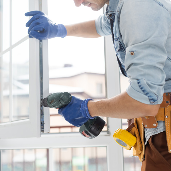 A worker wearing blue gloves uses a drill to install a window frame indoors in Mechanicsburg, PA